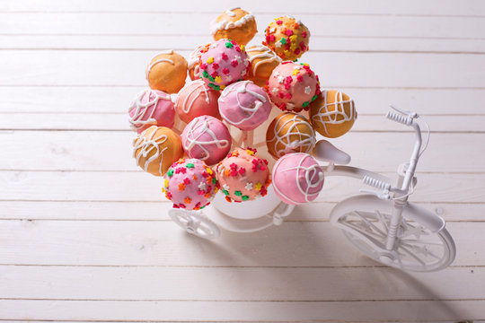 Cake pops  in decorative bicycle on white wooden background.