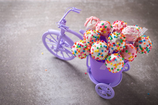 Cake pops  in decorative bicycle on grey slate  background.