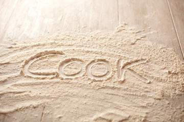 Kitchen table with flour and written word cook on it