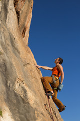 Young male climber hanging by a cliff.