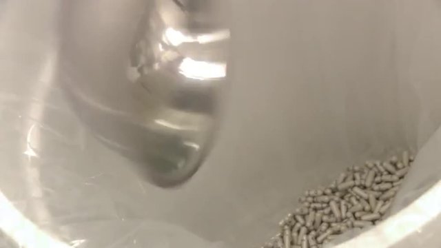 Closeup pan of a gloved hand scooping capsules.