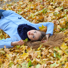 pretty sad dreamy girl lying among the leaves in the park