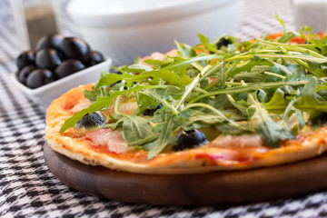 Homemade pizza with bacon, olives and arugula