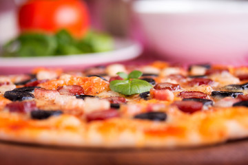 Homemade pizza with hunter sausages, bacon, olives and basil