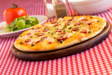 Homemade pizza with hunter sausages, bacon, peas and pickled cucumbers