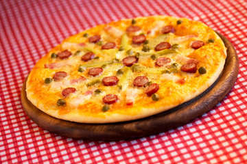 Homemade pizza with hunter sausages, bacon, peas and pickled cucumbers