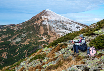 Fototapeta premium Female Hiker sitting on green Stone and using Thermos