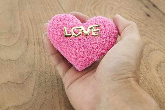 Hand holding pink heart on wood background