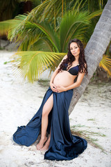 Young pregnant woman hugging tummy. Exotic nature, palm. Happy motherhood