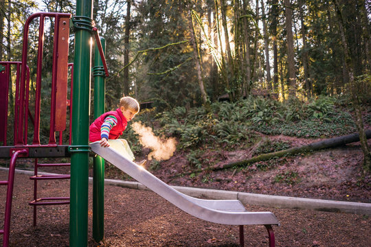 Boy on a slide in a park playground on a cold day breathing out
