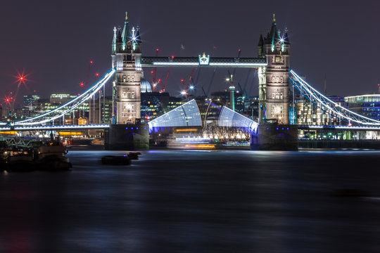 Tower Bridge at night opening with boat sailing below, London, England, UK
