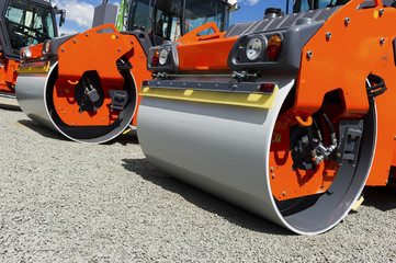 Steamroller, heavy road roller and vibration roller compactor in row on grey gravel, construction industry, blue sky and white clouds on background 