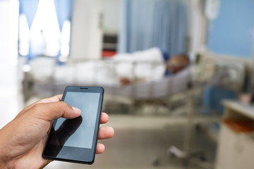 Hand hold and touch screen smart phone, tablet,cellphone on blur image of A patient in the hospital with saline intravenous, in Asian elderly man hand.