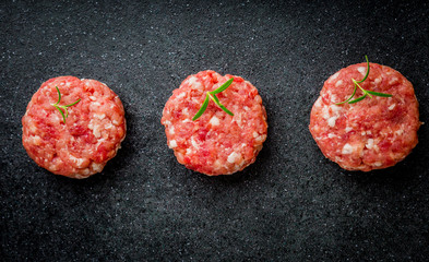 Raw burgers of beef and pork on a black board