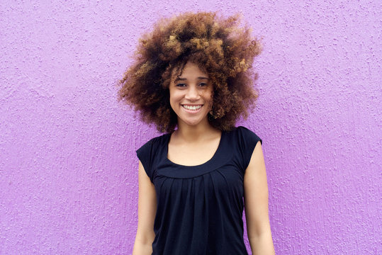 Smiling young woman with afro against purple background