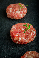 Raw burgers of beef and pork on a black board