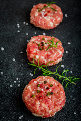 Raw burgers of beef and pork on a black board