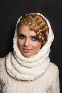 portrait of a beautiful young blonde woman on dark background. hair tied in a braid. girl wearing a warm sweater and scarf. copy space.