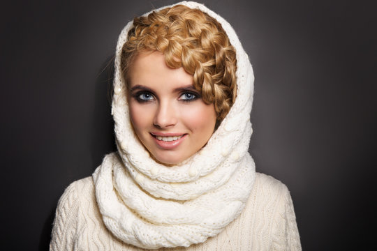 portrait of a beautiful young blonde woman on dark background. hair tied in a braid. girl wearing a warm sweater and scarf. copy space.