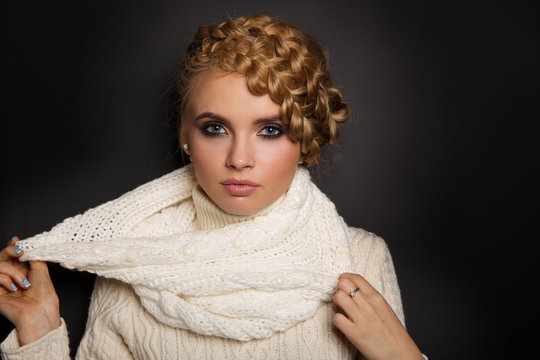 portrait of a beautiful young blonde woman on dark background. hair tied in a braid. girl wearing a warm sweater and scarf. copy space.