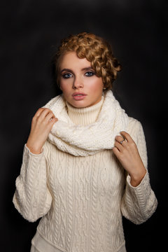 portrait of a beautiful young blonde woman on dark background. hair tied in a braid. girl wearing a warm sweater and scarf. copy space.
