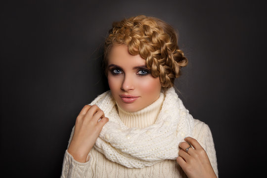 portrait of a beautiful young blonde woman on dark background. hair tied in a braid. girl wearing a warm sweater and scarf. copy space.