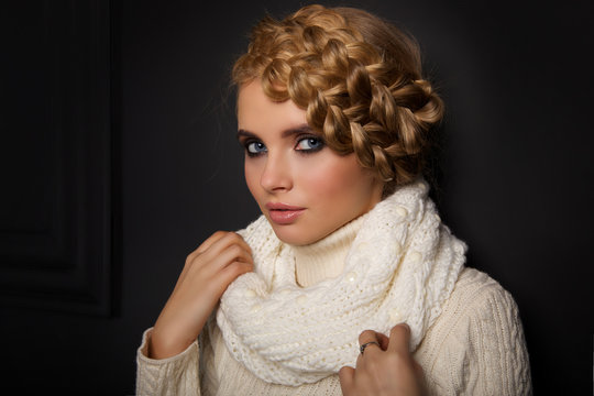 portrait of a beautiful young blonde woman on dark background. hair tied in a braid. girl wearing a warm sweater and scarf. copy space.