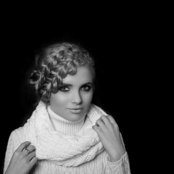 portrait of a beautiful young blonde woman on dark background. hair tied in a braid. girl wearing a warm sweater and scarf. copy space.