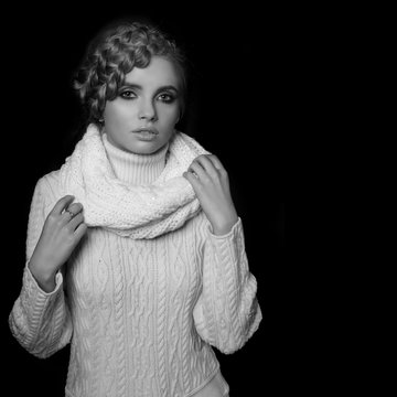portrait of a beautiful young blonde woman on dark background. hair tied in a braid. girl wearing a warm sweater and scarf. copy space.