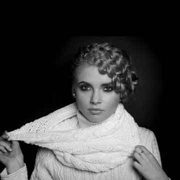 portrait of a beautiful young blonde woman on dark background. hair tied in a braid. girl wearing a warm sweater and scarf. copy space.