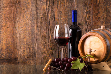 Glass of red wine with bottle barrel grapes and wooden backgroun