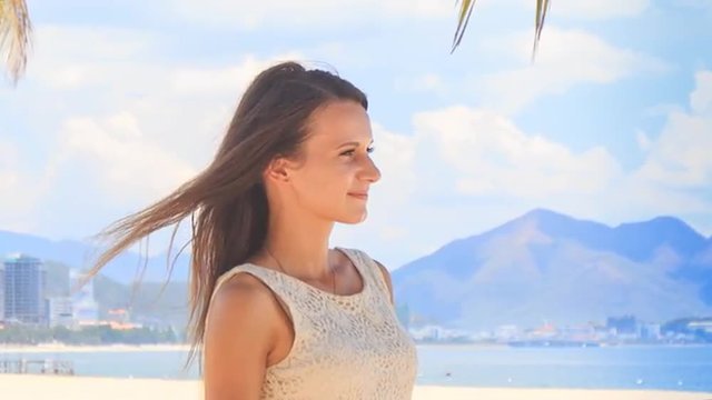 slim girl in white frock laughs lifts hands on beach