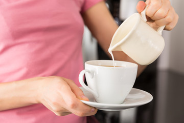 Woman adding milk to her coffee