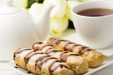 Eclairs and cup of tea on wooden table.