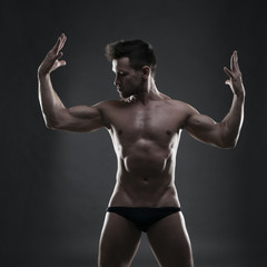 Fototapeta na wymiar Handsome muscular bodybuilder posing on gray background. Low key studio shot