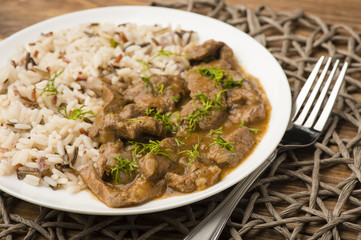 Stewed beef and rice on the white plate on wooden background.