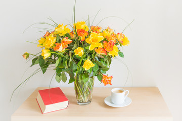 Bouquet of roses in a glass vase. Nearby is a book and a cup of black coffee