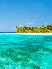 Maldives. Island in the ocean. Palm trees on the white sand beach. Turquoise water of the lagoon. Roof bungalow suite. Bleach Bypass effect.