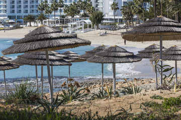 Detail of woven umbrellas above rows of many relaxing beds and l