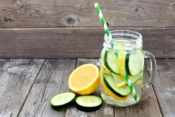 Keuken spatwand met foto Lemon cucumber detox water in a mason jar glass with straw and slices against a rustic wood background © Jenifoto