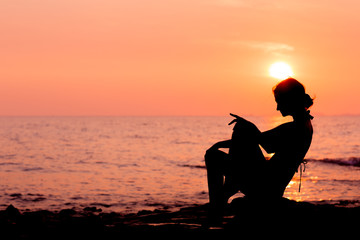 Woman silhouette sitting on sunset sea background, side view, back lit