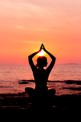 Woman silhouette sitting in lotus position on sunset sea background back lit