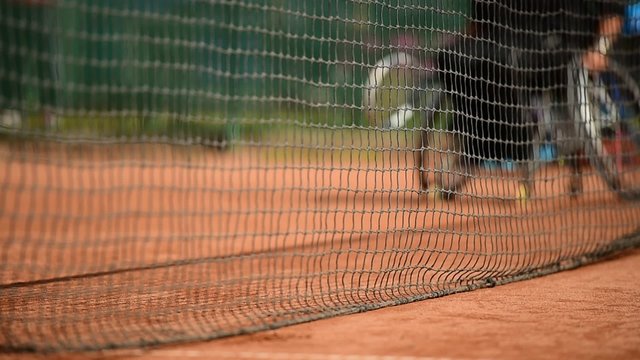 Wheelchair tennis player is seen behind the tennis net on a clay court