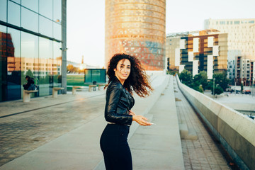 Portrait of a young attractive girl with long curly hair and a perfect figure on the background of urban buildings.