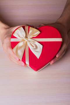 Two male hands holding red gift box in shape of heart