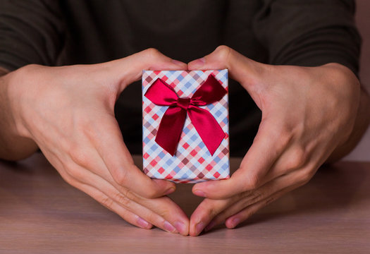 Two male hands in shape of heart holding checkered gift box with