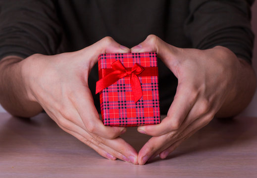 Two male hands in shape of heart holding red checkered gift box