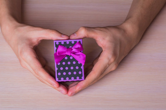 Two male hands in shape of heart holding purple spotted gift box