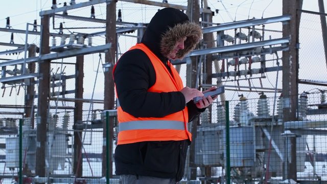 Electrician with tablet PC at power plant in winter