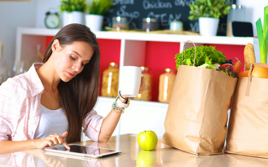 Woman using a tablet computer while drinking tea in her kitchen